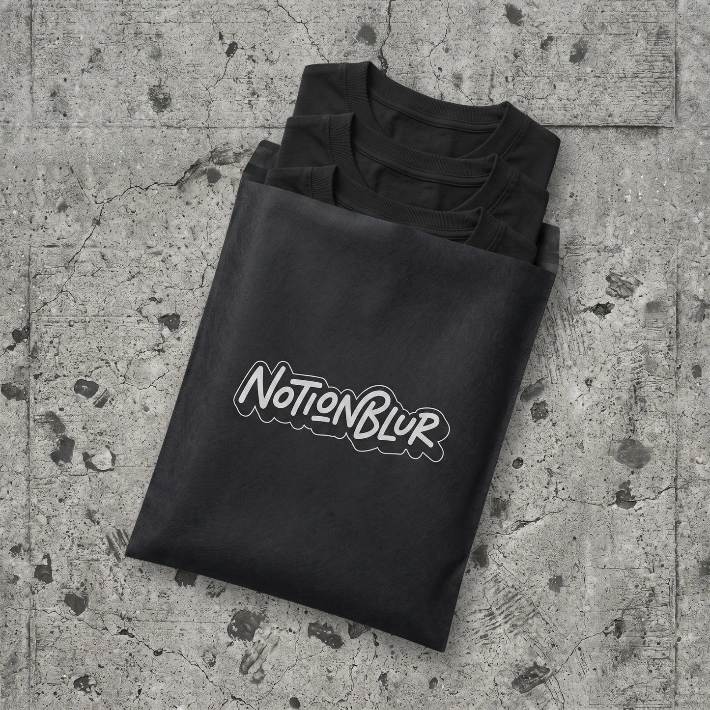Three folded Notionblur tees in a black mailer on city pavement
