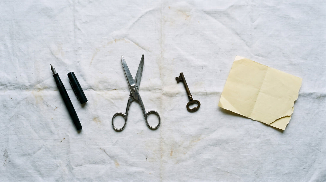 Overhead flat lay of a fountain pen, steel scissors, a brass key and a folded blank telegram on worn linen