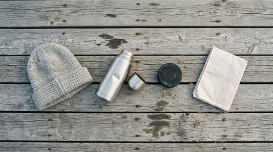Overhead flat lay of a wool toque, a steel flask, a hockey puck and a folded map on weathered dock boards