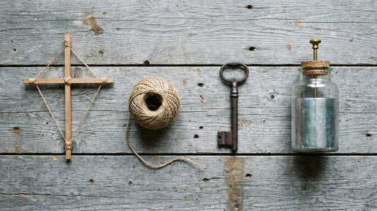 Overhead flat lay of lashed kite spars, a ball of twine, an iron key and a Leyden jar on weathered barn boards