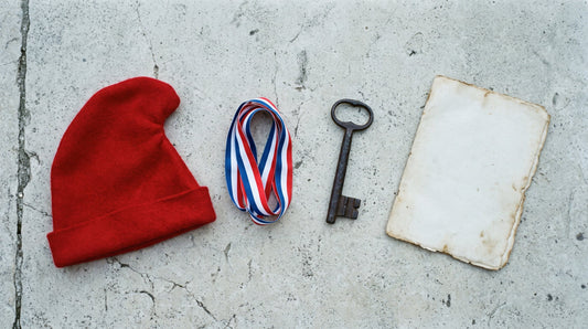 Overhead flat lay of a red Phrygian cap, a tricolour ribbon, an iron key and a folded blank sheet on limestone paving
