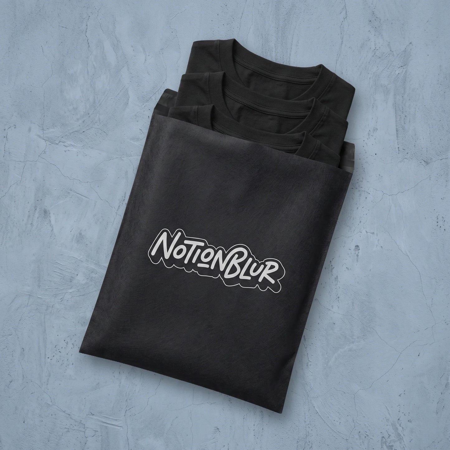 Three folded Notionblur tees in a black mailer on pale plaster