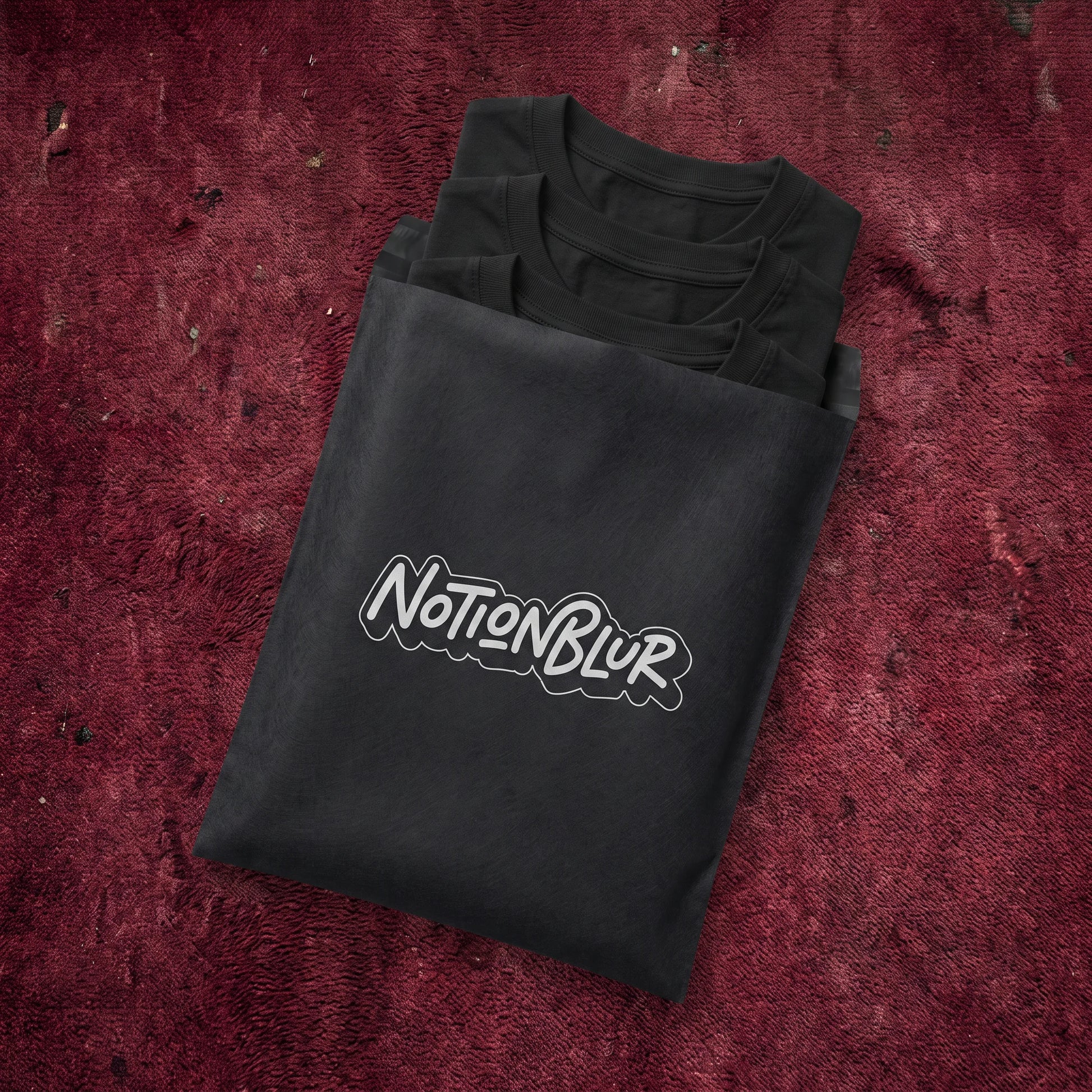 Three folded Notionblur tees in a black mailer on crimson cinema carpet