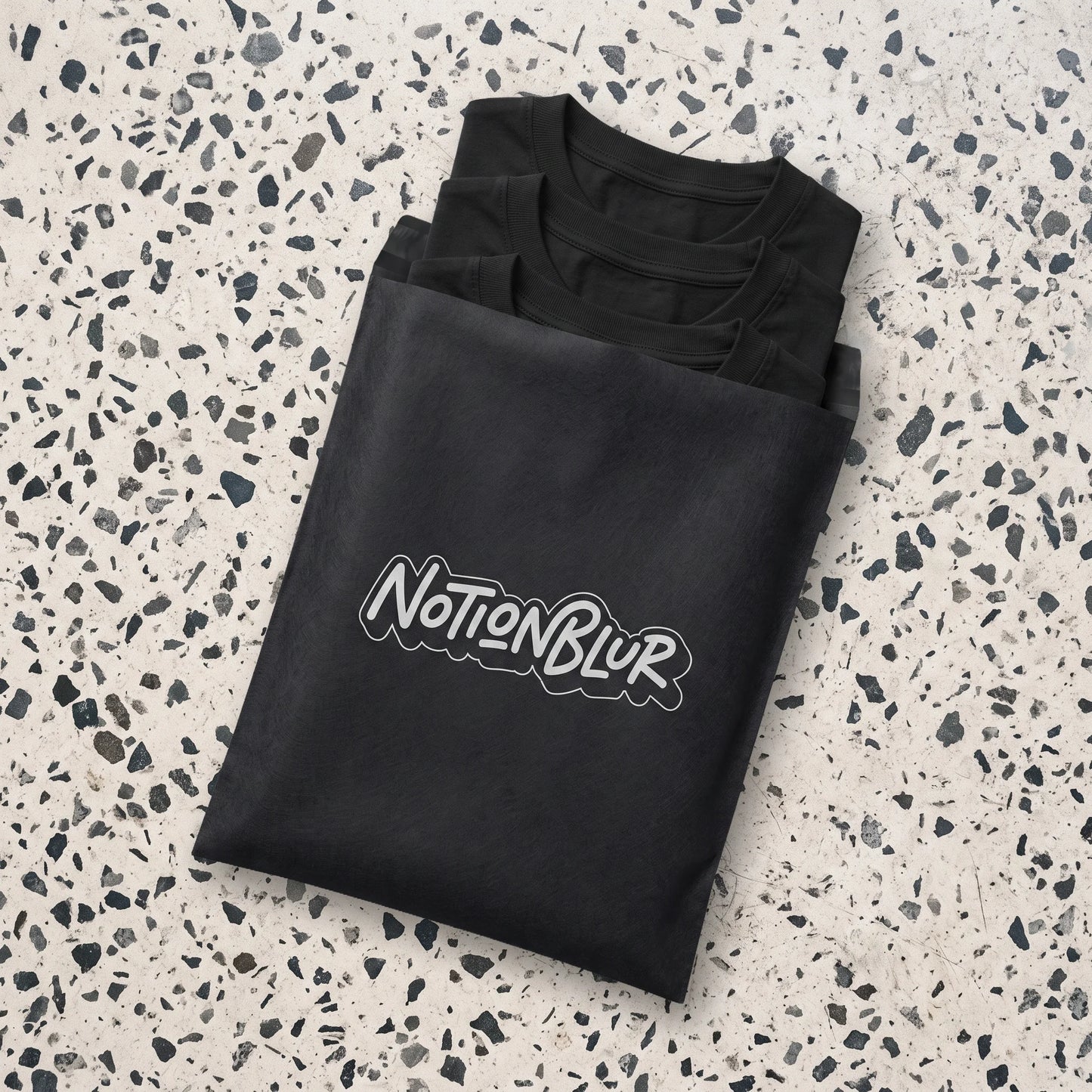 Three folded Notionblur tees in a black mailer on pale terrazzo