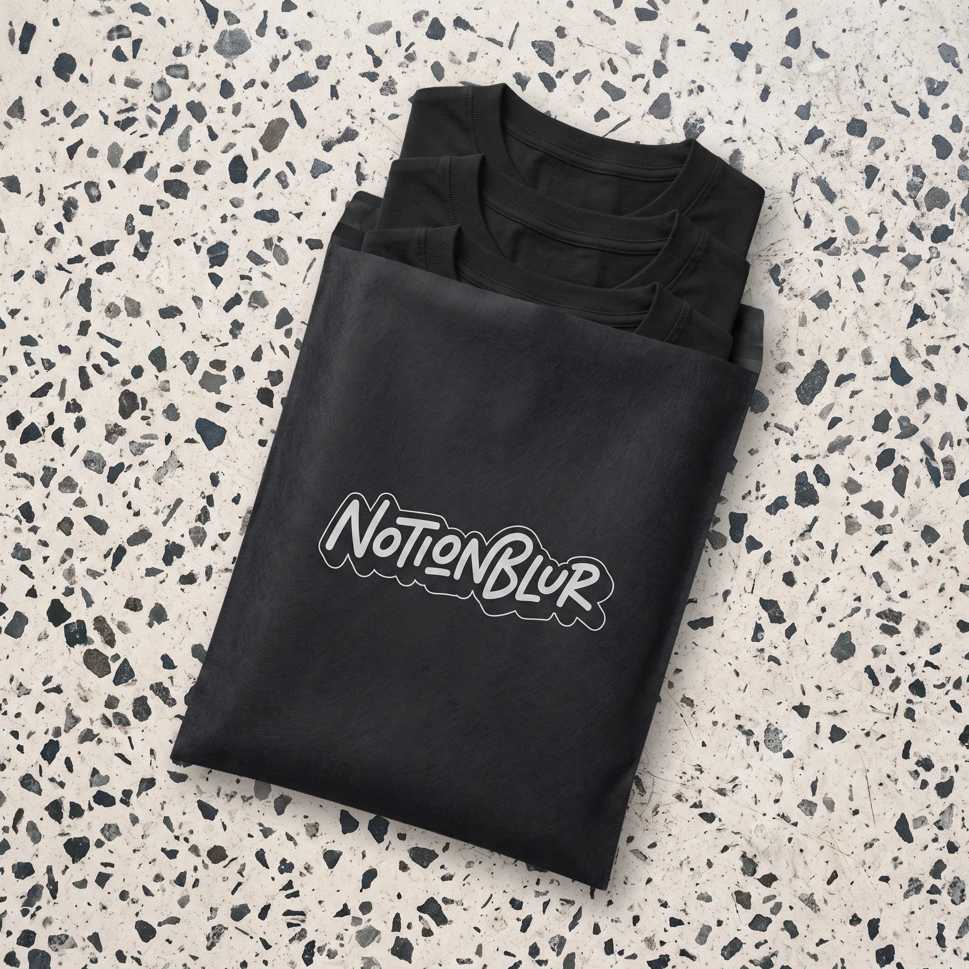 Three folded Notionblur tees in a black mailer on pale terrazzo