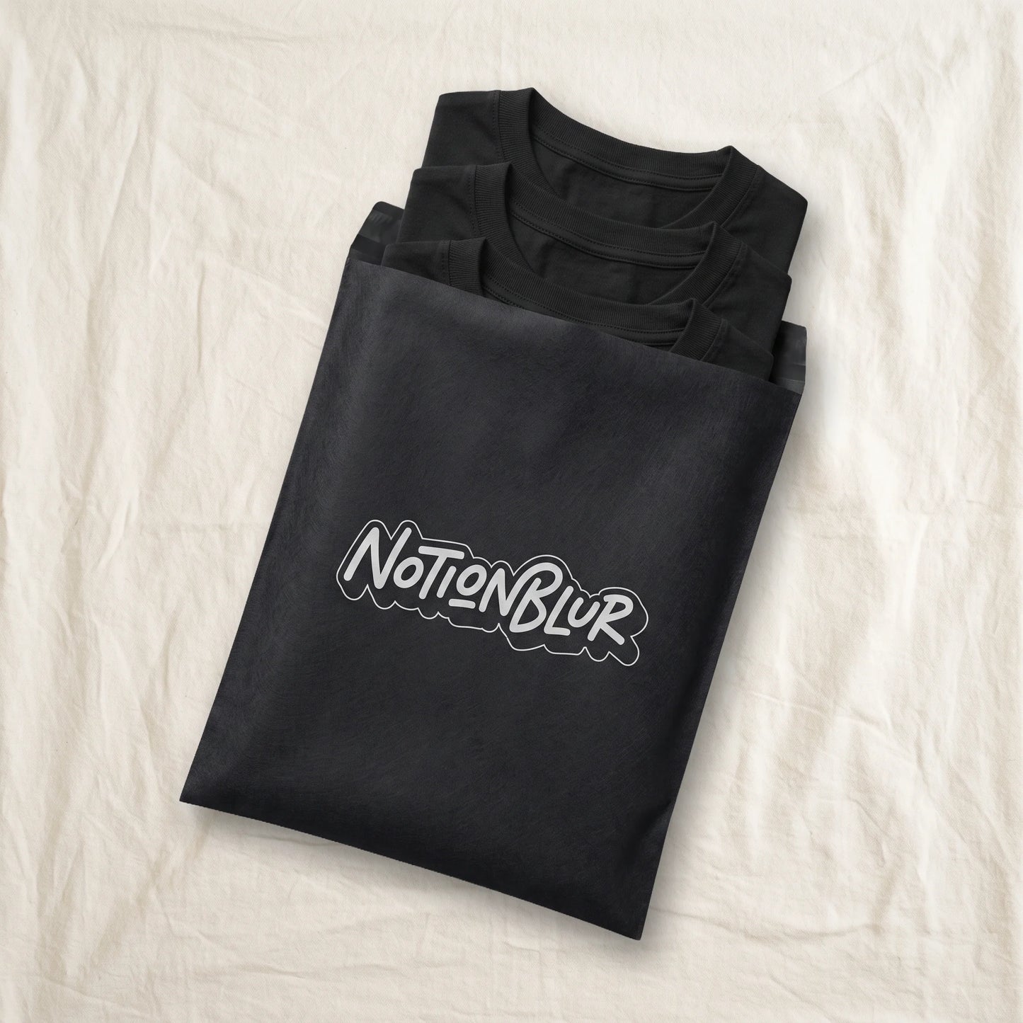 Three folded Notionblur tees in a black mailer on a rumpled cotton bedsheet